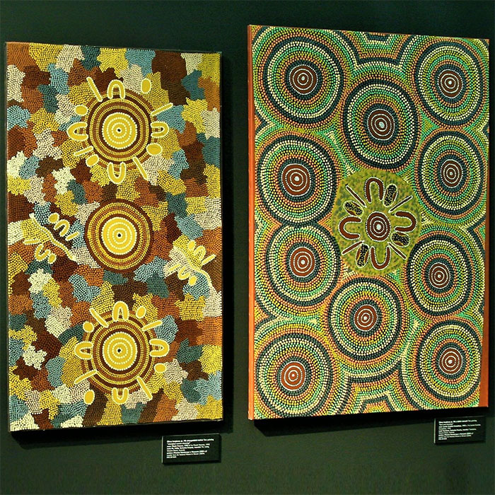 Dwa obrazy tzw. kropkowe utrzymane w kolorystyce pastelowej: brąz, biały, żółty, niebieski, zielony „Mit o dzikich ziarnach”, „Mit aborygeńskich kobiet”