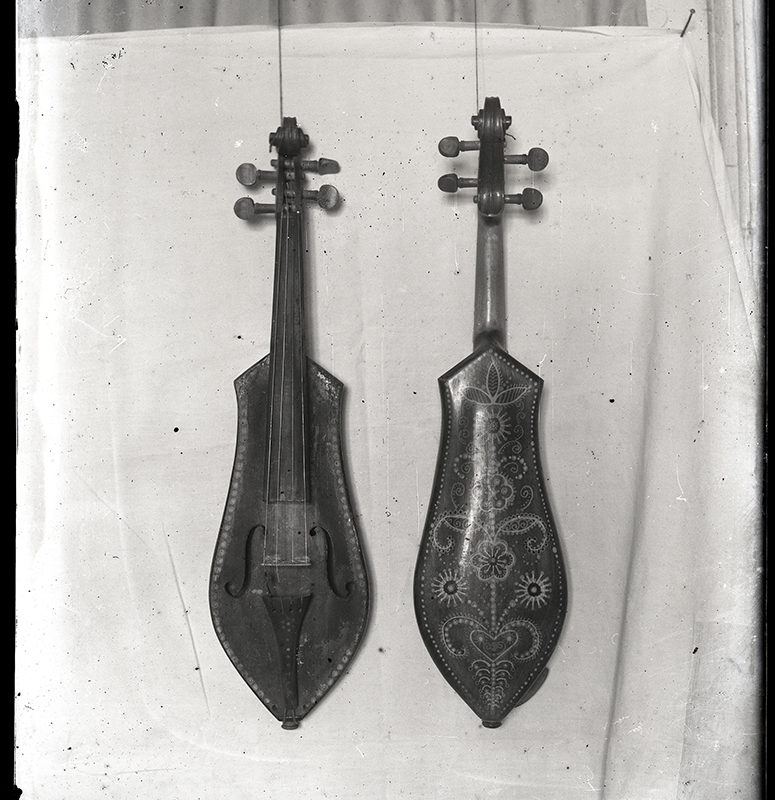 Instrumenty ludowe. Złóbcoki wykonane przez Józefa Zboźnia_Arch. PME N.4102 Zawieszone za szyjkę rzeźbione złóbcoki, na tle białej tkaniny. Z lewej strony ukazany jest przód instrumentu, z prawej strony tył.