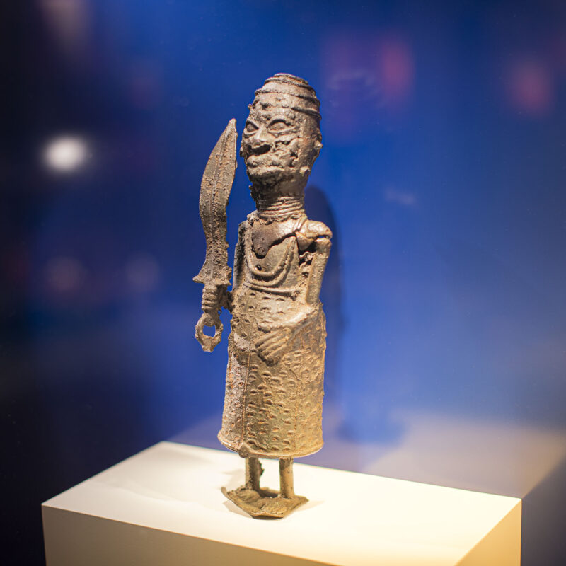 Widok wystawy. Na postumencie stoi wykonana z brązu figurka wojownika z Imperium Beninu.