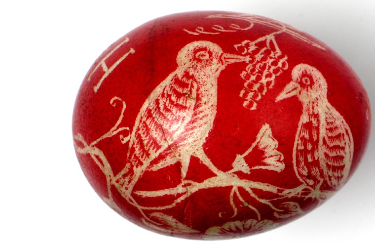 Pisanka rytowniczka barwiona na czerwono, wydrapano na niej wizerunek ptaszków na gałęzi.