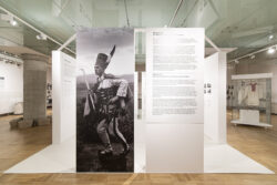 Widok na wejście na ekspozycje po lewej stronie duże powiększenie fotografii przedstawiającej Mieczysława Cholewę stojącego na pieńku w stroju podhalańskim z ciupagą w ręku i w zbójnickim kołpaku na głowie. Po prawej stornie tablica z tekstem dotyczącym wystawy.