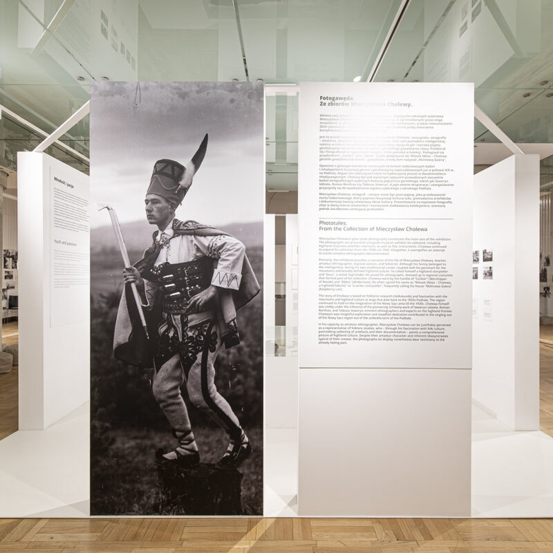 Widok na wejście na ekspozycje po lewej stronie duże powiększenie fotografii przedstawiającej Mieczysława Cholewę stojącego na pieńku w stroju podhalańskim z ciupagą w ręku i w zbójnickim kołpaku na głowie. Po prawej stornie tablica z tekstem dotyczącym wystawy.