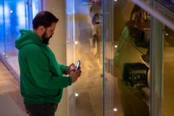 Mężczyzna stoi przy szklanej gablocie na wystawie i robi zdjęcie eksponatom za szybą.