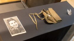 Na zdjęciu widać obiekty w gablocie na wystawie. W gablocie znajduje się czarno biała fotografia, srebrny orzełek przypinka oraz brezentowy przybornik.