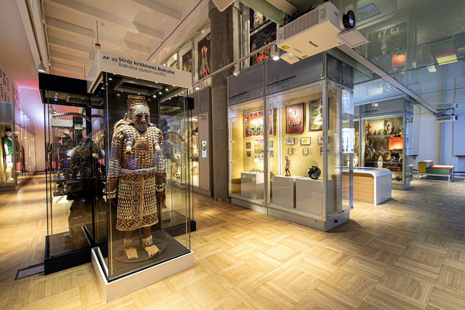 Widok wystawy. W szklanych gablotach obiekty z Afryki. W gablocie na pierwszym planie strój królowej Bakuba zdobiony graficznym wzorem.